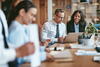 Coworkers look at laptop in office with wooden desk
